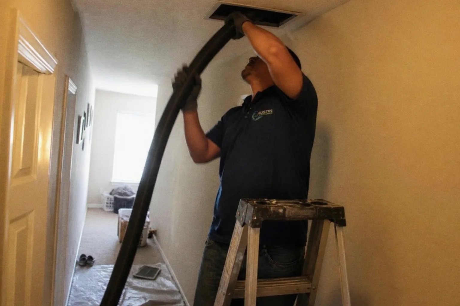 Austin Air Duct Cleaning technician cleaning a ceiling air vent in a hallway
