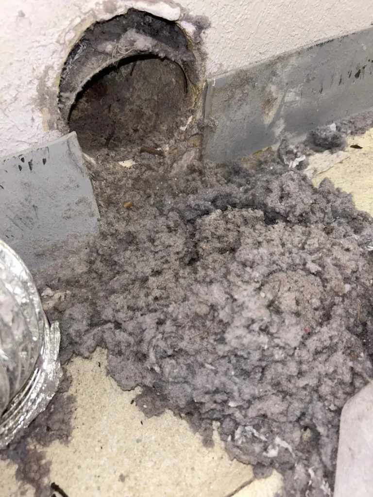 Packed lint pouring out of a clogged dryer vent opening