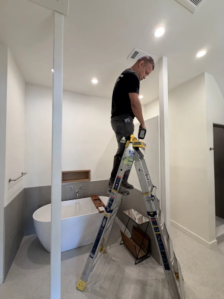 Technician cleaning a bathroom ceiling vent from a ladder
