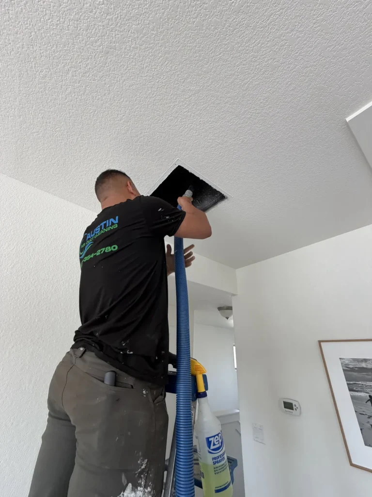 Technician cleaning a ceiling supply vent with a vacuum hose in an Austin home