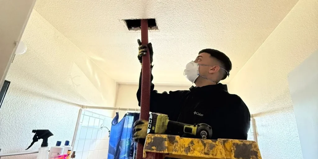 Technician cleaning a ceiling vent from a ladder