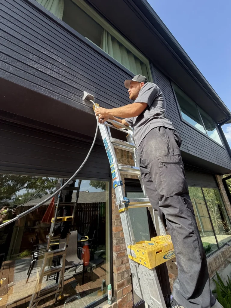 Technician cleaning an exterior dryer vent from a ladder on a two-story home