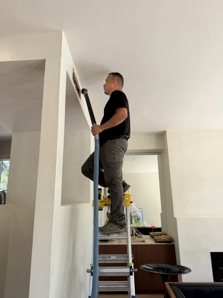 Technician on a ladder cleaning a ceiling supply duct