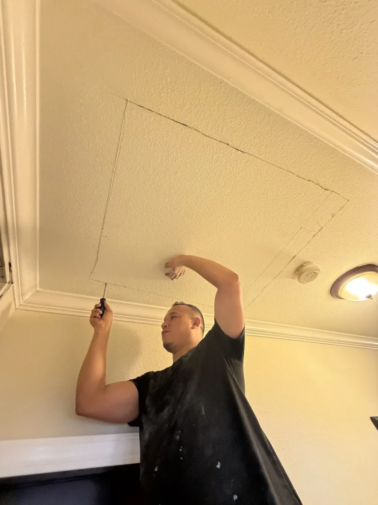 Technician working on a ceiling access panel in a home